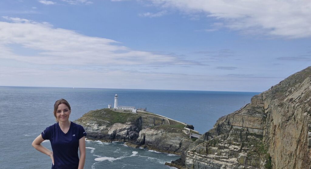 menyw yn sefyll o flaen goleudy Ynys Lawd yn Ynys Môn